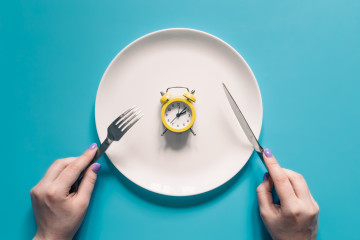 Manos sosteniendo un cuchillo y un tenedor sobre el despertador en un plato sobre fondo azul
