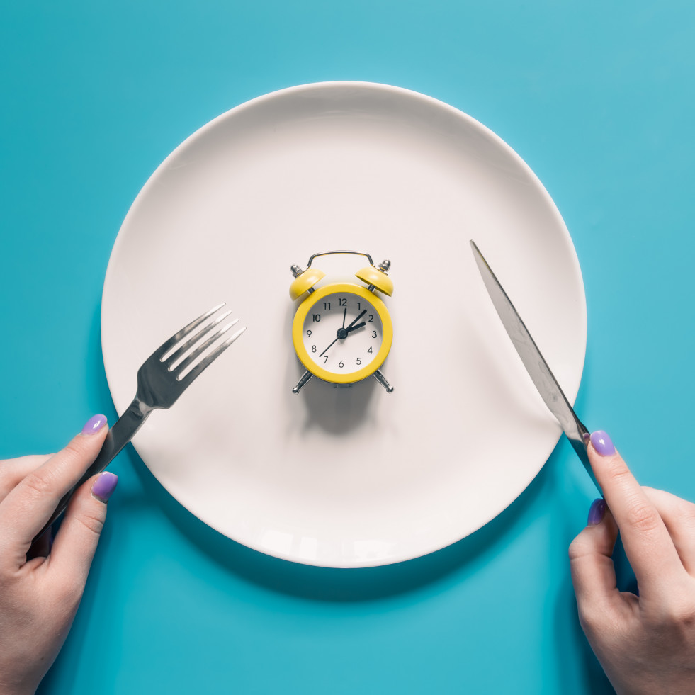 Manos sosteniendo un cuchillo y un tenedor sobre el despertador en un plato sobre fondo azul